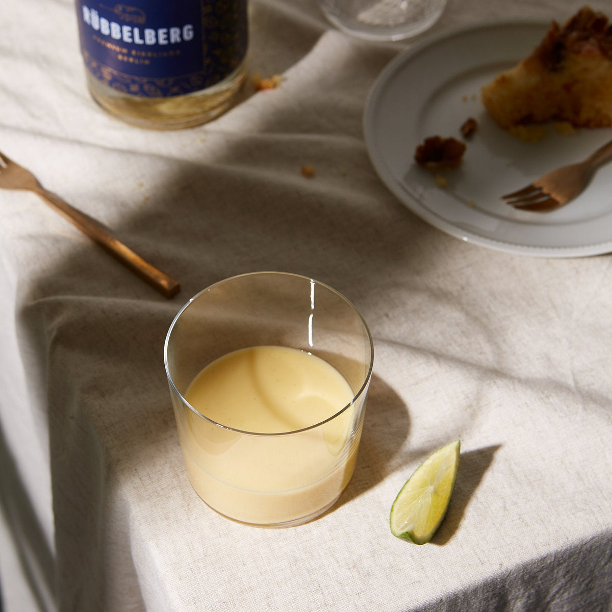 Flasche Rübbelberg Bio-Eierlikör mit einem Glas und Limetten auf einem gedeckten Tisch