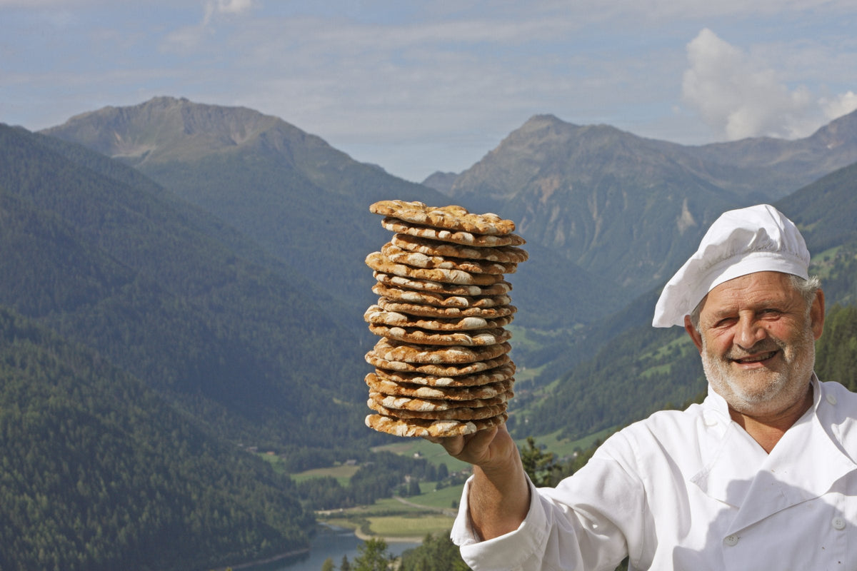 Bäckermeister Richard Schwienbacher hält einen Stapel Schüttelbrot vor den Bergen des Ultentals